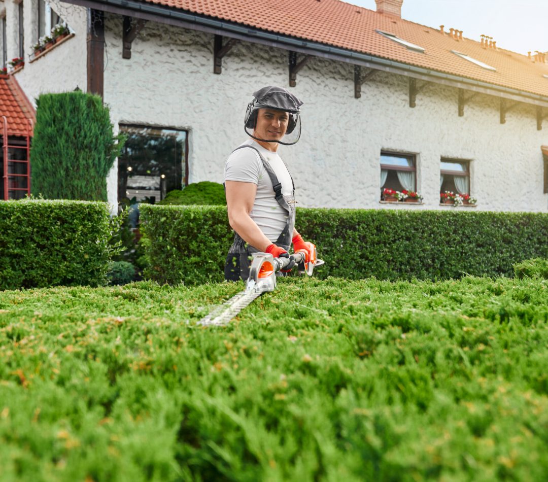 Man in uniform, glasses and gloves pruning bushes at garden